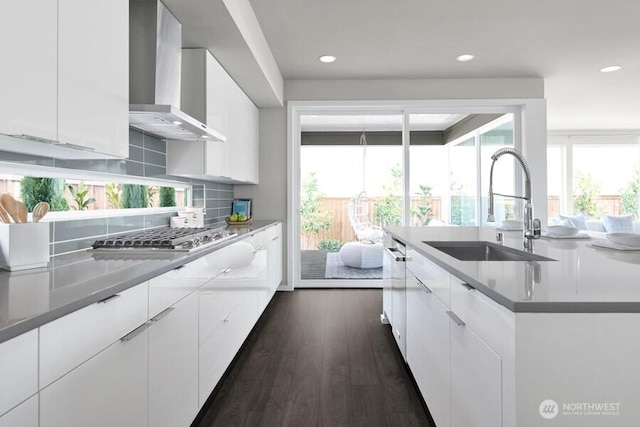 kitchen with a sink, backsplash, wall chimney range hood, stainless steel gas stovetop, and dark wood-style flooring