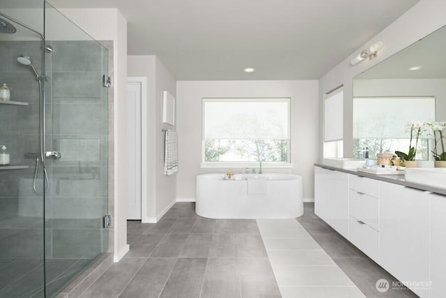 full bathroom featuring vanity, baseboards, a stall shower, a freestanding bath, and tile patterned flooring