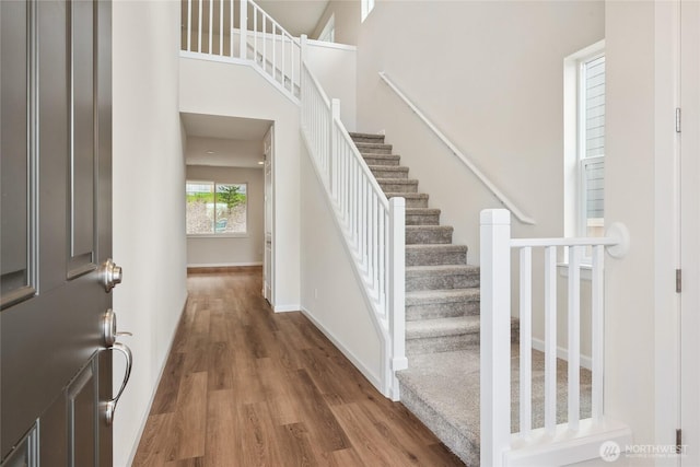 entryway with a towering ceiling, baseboards, wood finished floors, and stairs