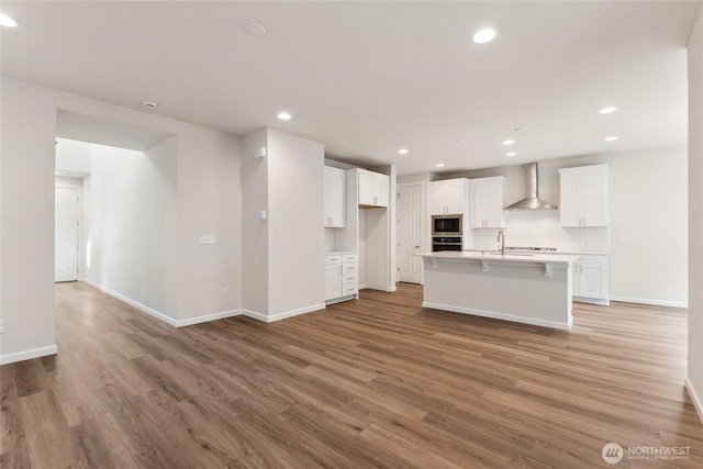 kitchen featuring wall chimney range hood, light wood-type flooring, light countertops, appliances with stainless steel finishes, and white cabinetry