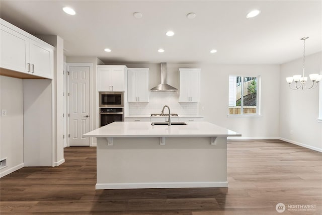 kitchen featuring wood finished floors, light countertops, appliances with stainless steel finishes, wall chimney range hood, and backsplash