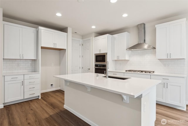 kitchen with a sink, appliances with stainless steel finishes, dark wood-style flooring, and wall chimney range hood