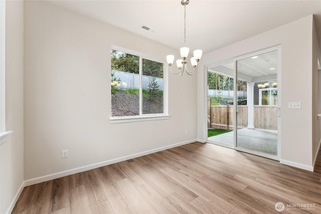 unfurnished room featuring visible vents, plenty of natural light, an inviting chandelier, and wood finished floors