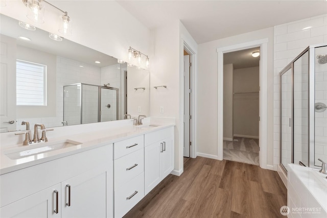 bathroom with double vanity, a stall shower, wood finished floors, and a sink