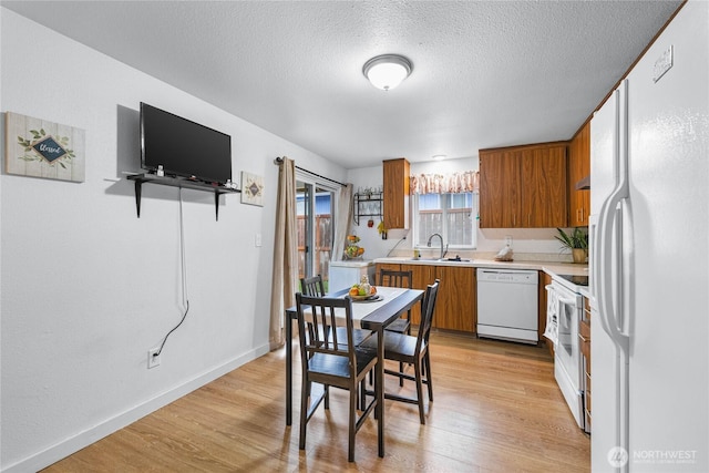 kitchen featuring white appliances, light wood finished floors, a sink, light countertops, and brown cabinets