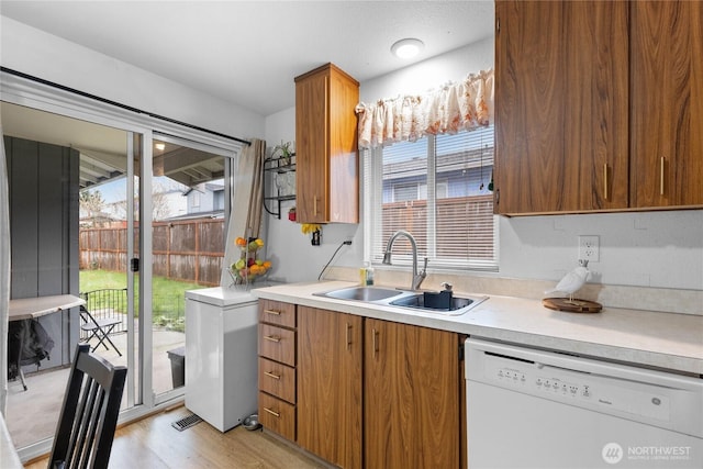 kitchen with light wood finished floors, dishwasher, light countertops, brown cabinetry, and a sink