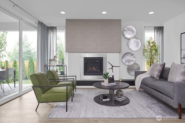 living area with a glass covered fireplace, wood finished floors, and recessed lighting