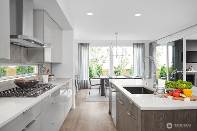 kitchen featuring stainless steel appliances, a sink, wall chimney range hood, modern cabinets, and backsplash