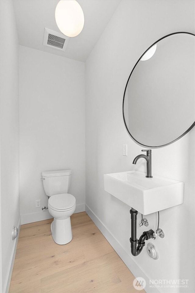 bathroom with visible vents, toilet, baseboards, and wood finished floors