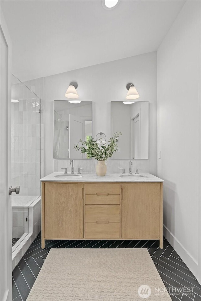 bathroom with double vanity, baseboards, a tile shower, and a sink