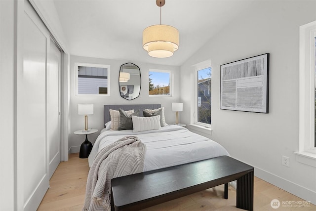 bedroom with a closet, baseboards, lofted ceiling, and light wood-style floors