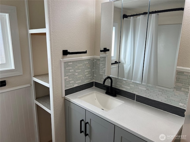 bathroom featuring vanity, wainscoting, and a textured wall