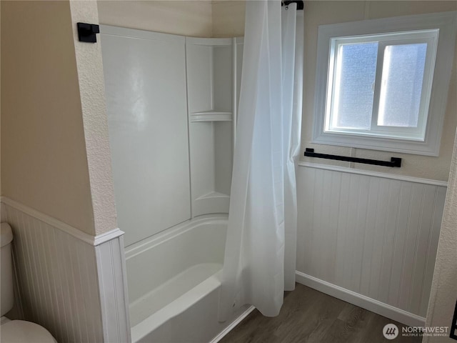 full bath featuring a wainscoted wall, toilet, shower / tub combo, and wood finished floors