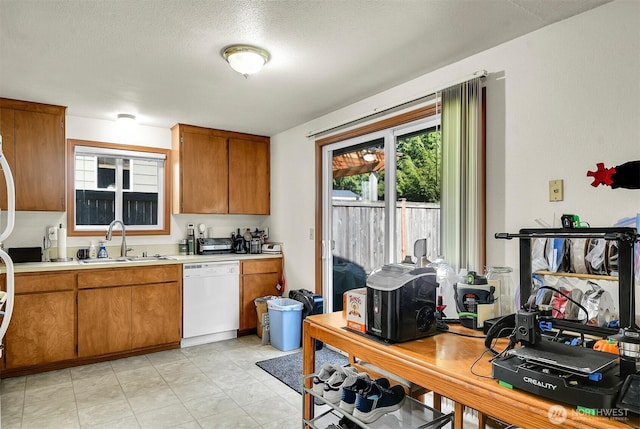 kitchen with brown cabinets, a sink, plenty of natural light, white dishwasher, and light countertops