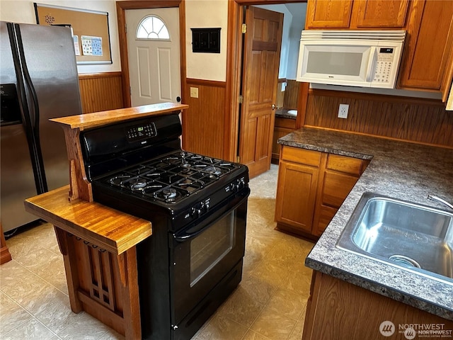 kitchen featuring white microwave, stainless steel fridge with ice dispenser, black gas range, a wainscoted wall, and a sink