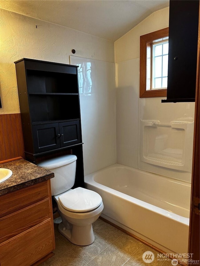 bathroom with vanity, vaulted ceiling, toilet, and a textured wall