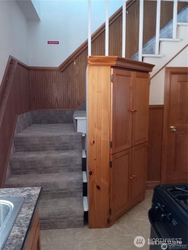 stairs with tile patterned floors, wood walls, and wainscoting