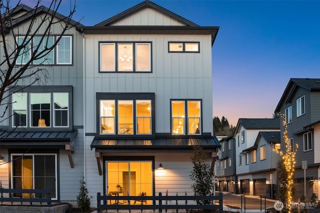 back of house at dusk with a standing seam roof, board and batten siding, and metal roof