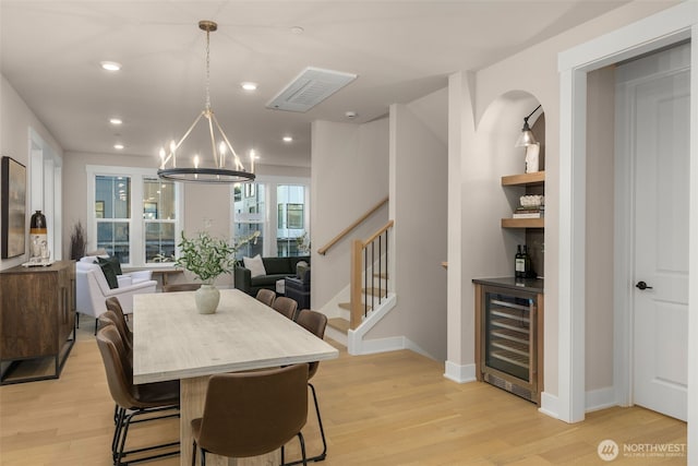 dining area featuring an inviting chandelier, beverage cooler, stairs, and light wood finished floors