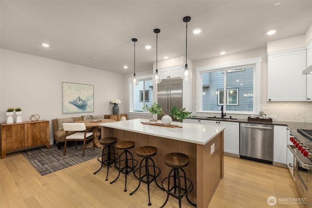 kitchen with high quality appliances, light wood-style flooring, a sink, a kitchen island, and white cabinets