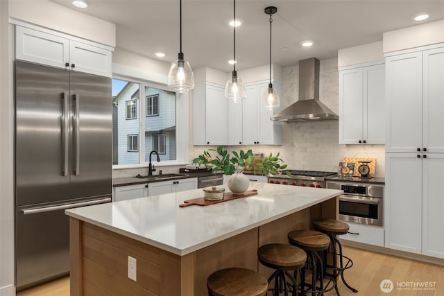 kitchen featuring a kitchen island, a sink, stainless steel appliances, wall chimney exhaust hood, and backsplash