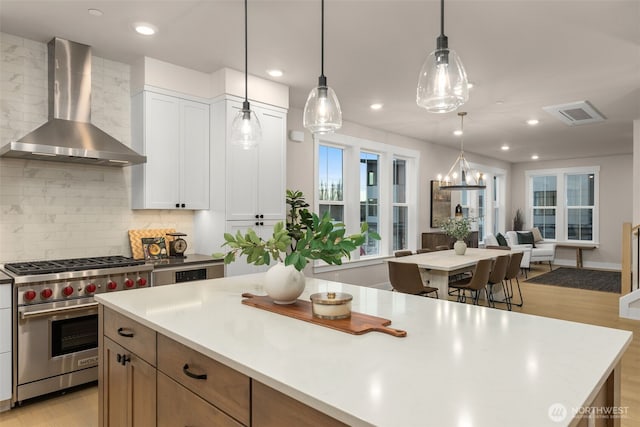 kitchen featuring a center island, wall chimney range hood, open floor plan, decorative backsplash, and designer stove