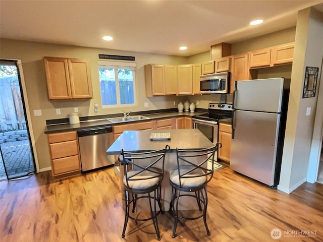 kitchen featuring light brown cabinetry, a sink, dark countertops, stainless steel appliances, and light wood finished floors