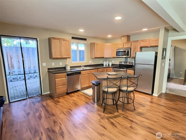 kitchen with dark countertops, light brown cabinetry, appliances with stainless steel finishes, wood finished floors, and a sink