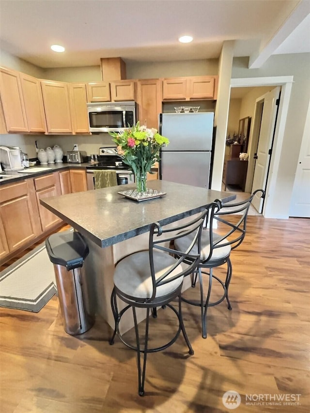 kitchen featuring dark countertops, light brown cabinets, stainless steel appliances, and light wood-style floors