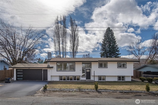 bi-level home with driveway, a chimney, a front yard, and fence