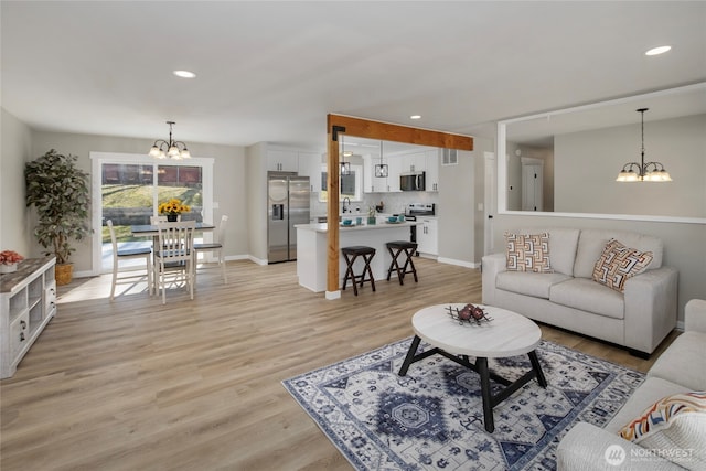 living room with light wood finished floors, a notable chandelier, recessed lighting, and baseboards