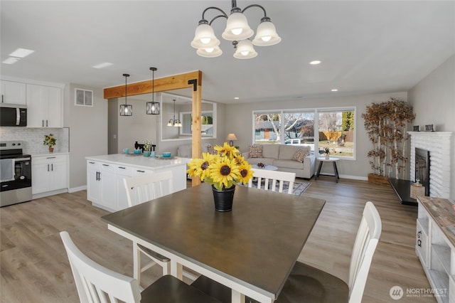 dining space with visible vents, light wood-style flooring, a fireplace, baseboards, and a chandelier