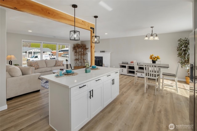 kitchen featuring a brick fireplace, open floor plan, light countertops, light wood-style flooring, and white cabinetry