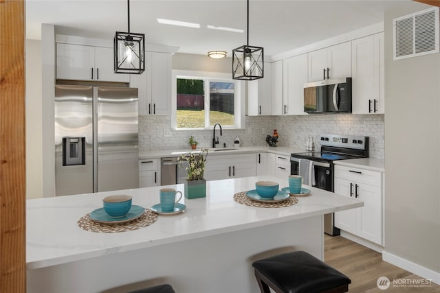 kitchen featuring a breakfast bar, visible vents, stainless steel appliances, and a sink