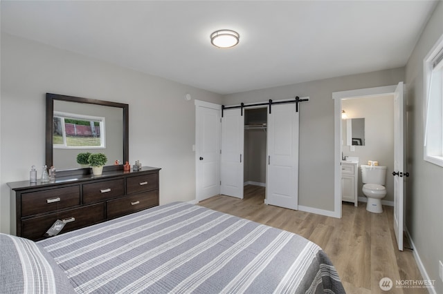 bedroom featuring baseboards, light wood-style flooring, a closet, ensuite bathroom, and a barn door