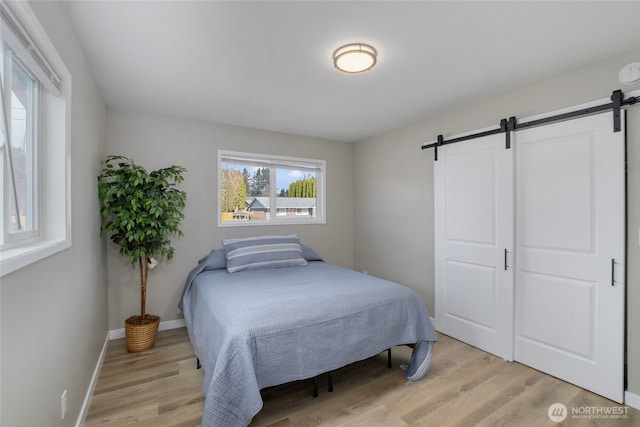 bedroom with a barn door, light wood-style flooring, and baseboards