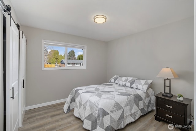 bedroom with a barn door, baseboards, and wood finished floors