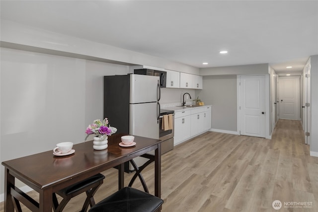 kitchen with stainless steel range with electric stovetop, freestanding refrigerator, light wood-style floors, white cabinetry, and a sink