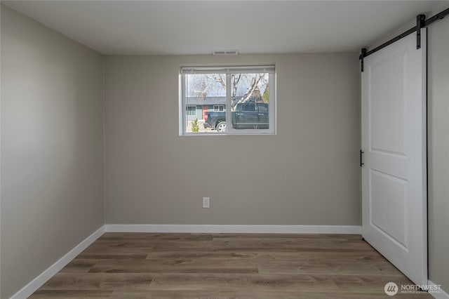 unfurnished room featuring visible vents, baseboards, a barn door, and wood finished floors