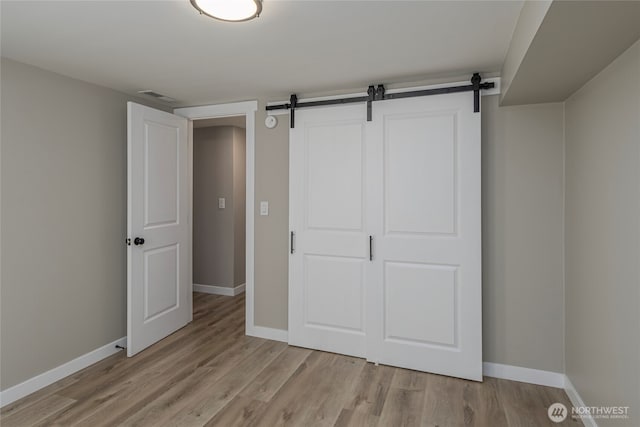 unfurnished bedroom featuring a barn door, baseboards, visible vents, and light wood-type flooring