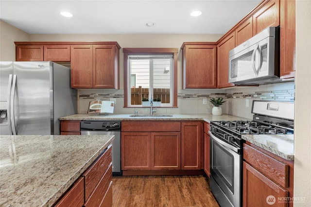 kitchen featuring a sink, tasteful backsplash, wood finished floors, appliances with stainless steel finishes, and light stone countertops