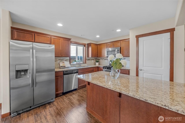 kitchen with light stone counters, dark wood-style floors, appliances with stainless steel finishes, brown cabinetry, and decorative backsplash