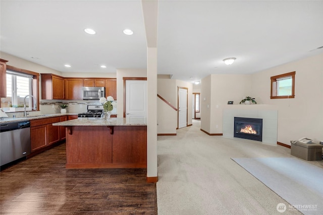 kitchen featuring open floor plan, light stone counters, appliances with stainless steel finishes, a kitchen breakfast bar, and a sink