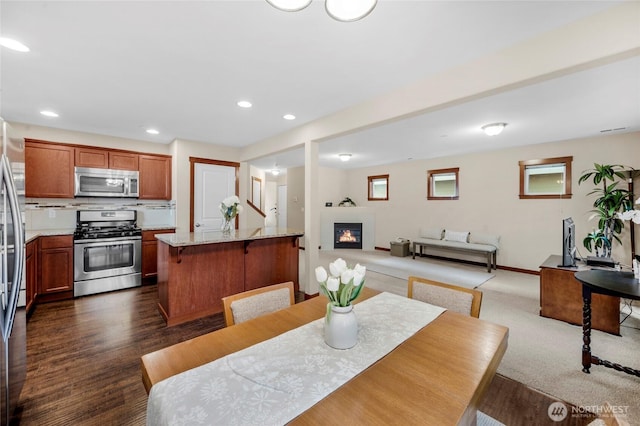 dining area featuring a glass covered fireplace, recessed lighting, dark wood-type flooring, and baseboards