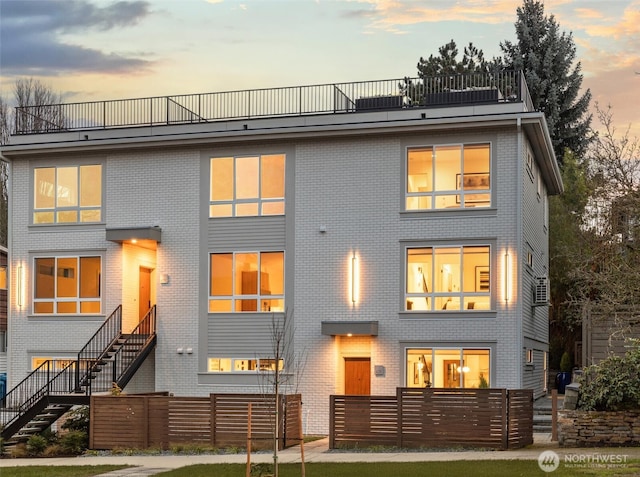 back of property at dusk with stairs, brick siding, and a fenced front yard