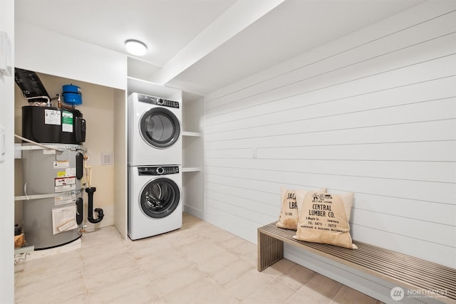 laundry room with strapped water heater, laundry area, and stacked washer and dryer