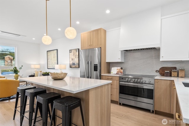 kitchen featuring a kitchen island, decorative backsplash, light wood-style floors, appliances with stainless steel finishes, and a kitchen breakfast bar