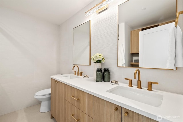 full bathroom with a sink, toilet, tile walls, and double vanity