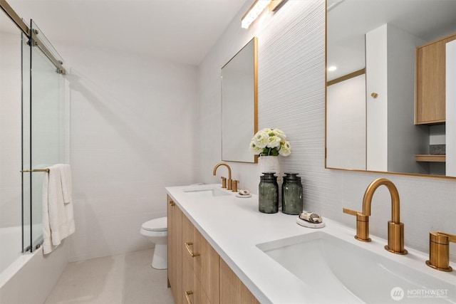 bathroom with double vanity, toilet, tile walls, and a sink