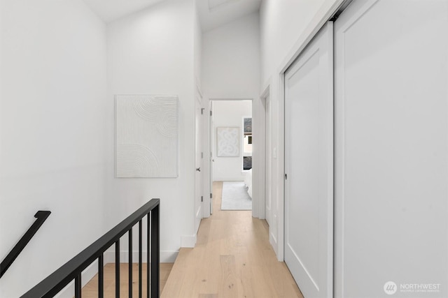 corridor featuring an upstairs landing, light wood-style floors, and a high ceiling